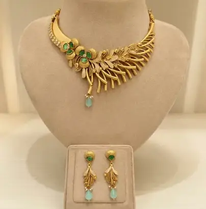Feather motif gold necklace with matching earrings on cream busts
