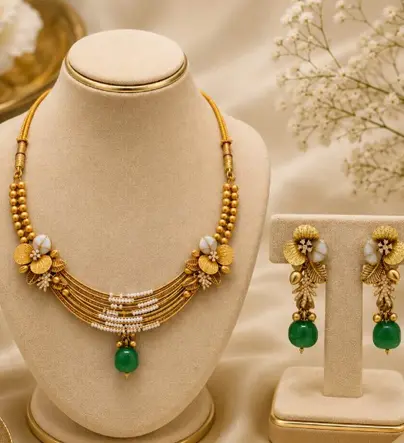 Gold and pearl necklace with green drop earrings on cream busts